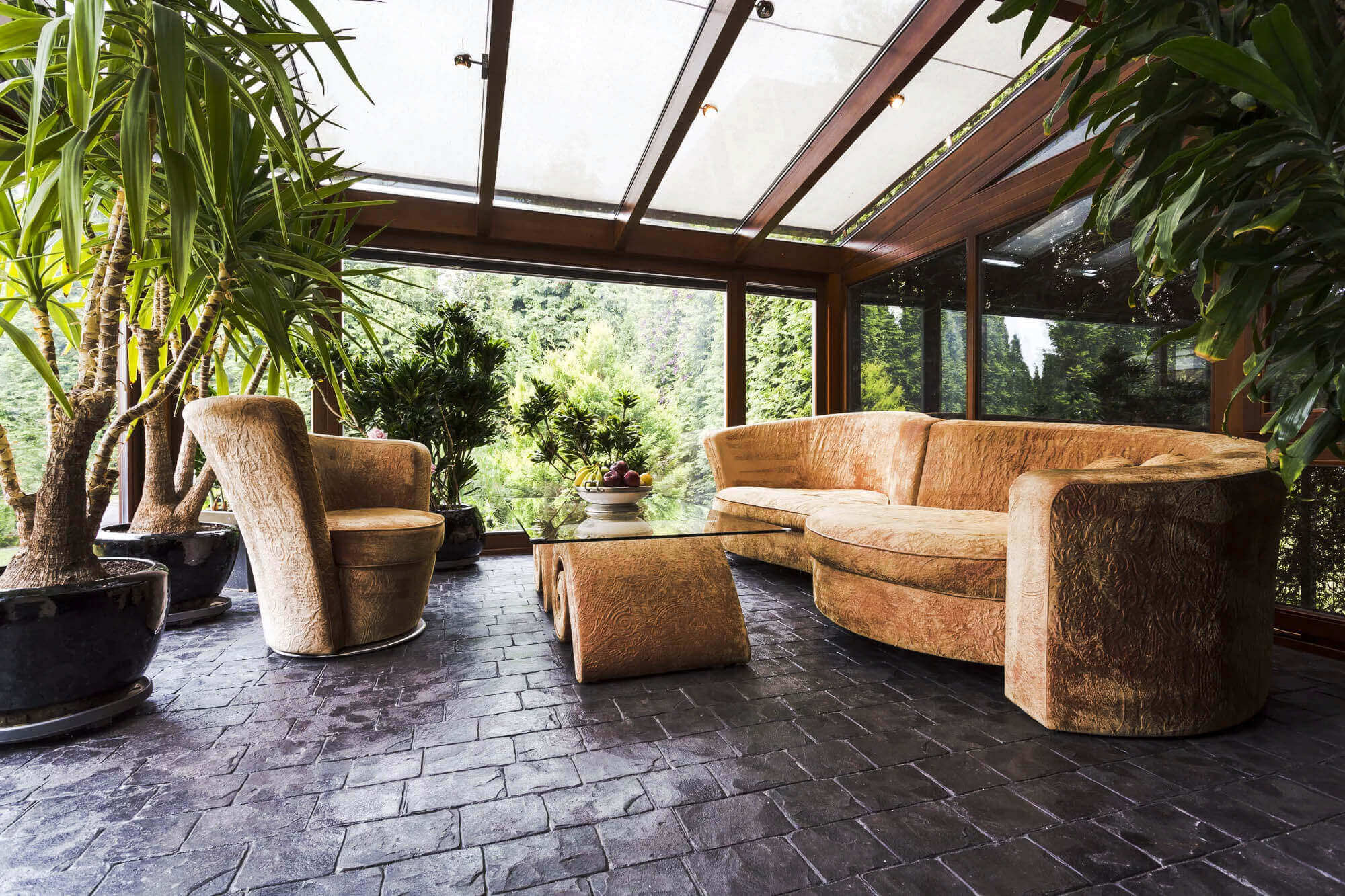 Luxus-Kaltwintergarten mit braunen Sofas, Glastisch und großen Pflanzen; alles direkt am Haus